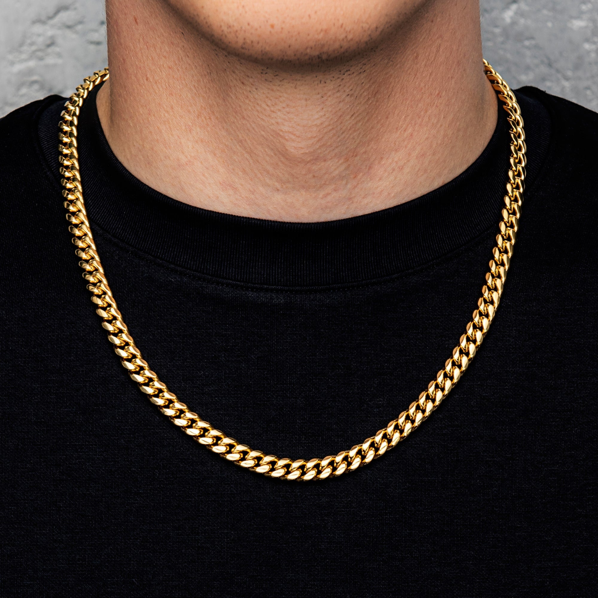 Gold chain necklace worn by a person on a black shirt with a gray background
